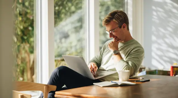 Ein Mann füllt in seinem Zuhause, lächelnd und bequem neben seinem Schreibtisch sitzend, das Datenänderungsformular online aus.